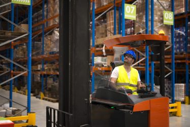 Forklift driver relocating and lifting goods in large warehouse center.